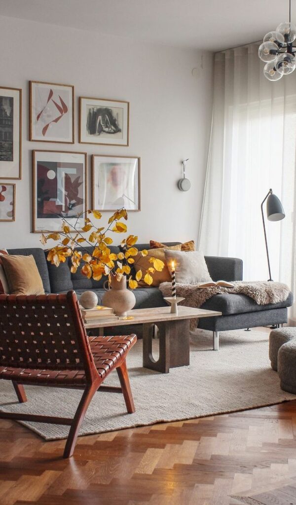 Colori naturali protagonisti nel living, con il divano antracite sul tappeto panna e i rami di foglie gialle in un vaso