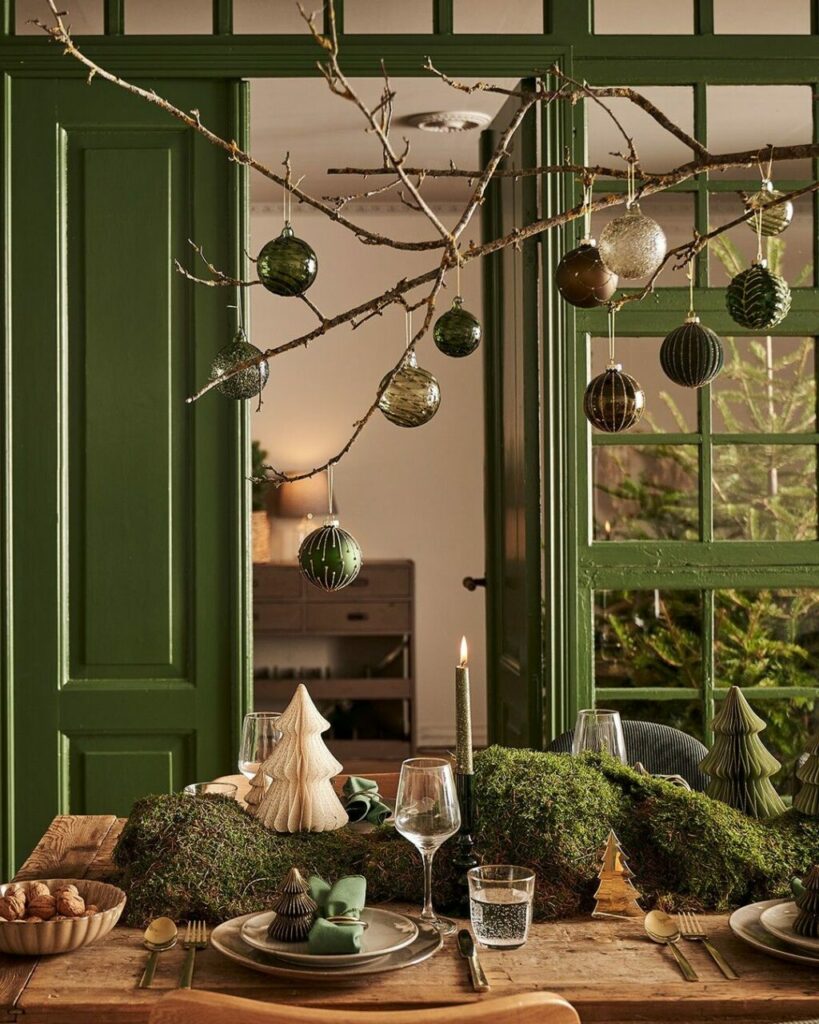 Muschio, candele, palline e alberelli in una tavola di Natale giocata sui colori del legno e delle piante