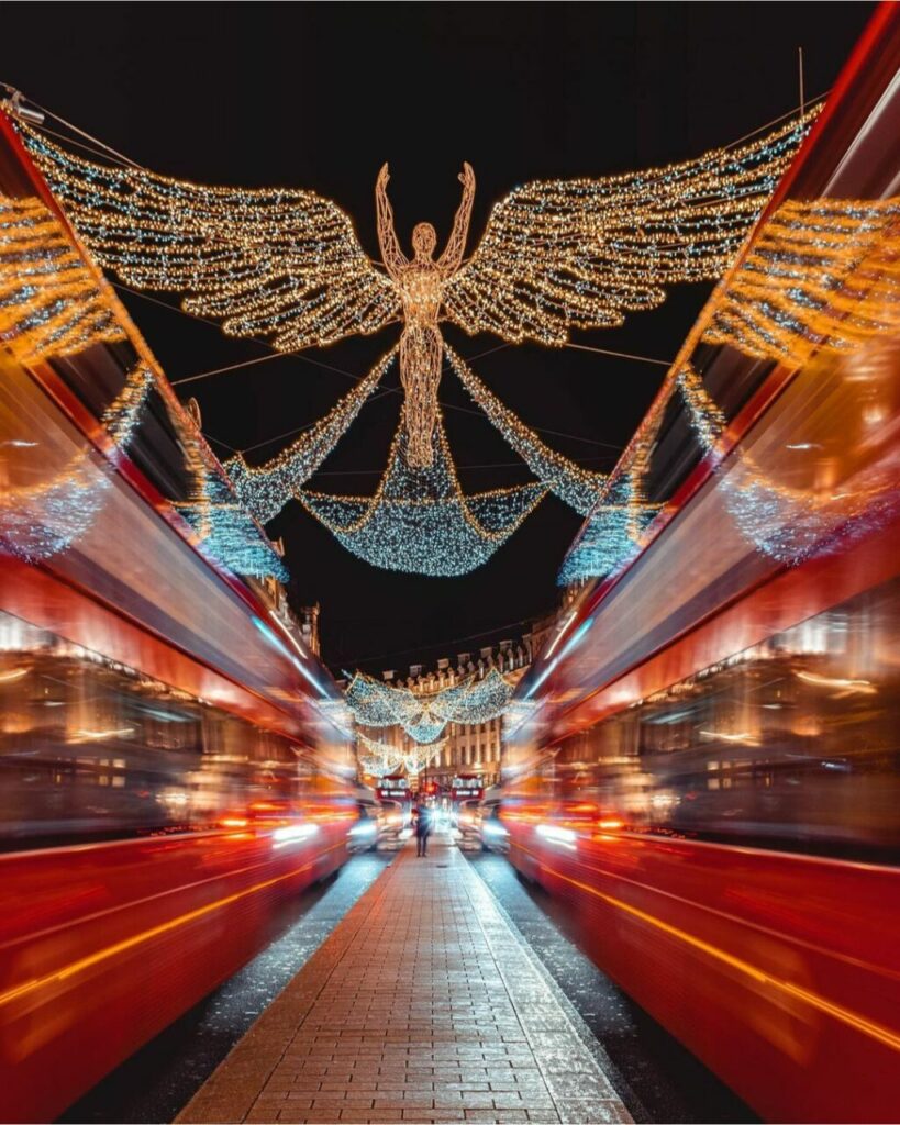 Due bus rossi sfrecciano su Regent Street, sovrastati da angeli luminosi