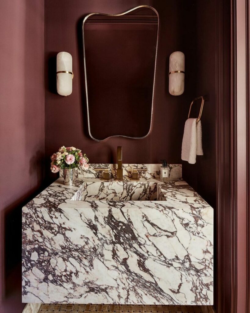 Uno specchio del bagno dal contorno irregolare in contrasto con un lavandino monolitico in marmo